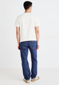 Lys beige bomulls t-skjorte, kort erm, rund hals. Blå denim jeans, rett passform, baklommer, brune sneakers med hvite detaljer.