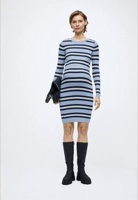 Ριγέ εφαρμοστό πλεκτό φόρεμα σε ανοιχτό γαλάζιο και ναυτικό μπλε, με μακριά μανίκια και στρογγυλή λαιμόκοψη, συνδυασμένο με μαύρες μπότες μέχρι το γόνατο και μαύρο μπουφάν.