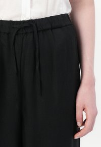 Black, lightweight, elastic waistband pants with a drawstring tie. Smooth texture, wide-leg design, paired with a white button-up shirt.