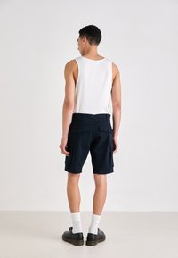Shorts cargo de marine en mélange de coton, avec plusieurs poches, une coupe droite et une taille avec passants de ceinture. Associés à un débardeur blanc et des chaussettes.