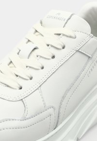 Gros plan d'une basket en cuir blanc avec semelle texturée, lacets blancs et inscription "Copenhagen" sur la languette et le panneau latéral.