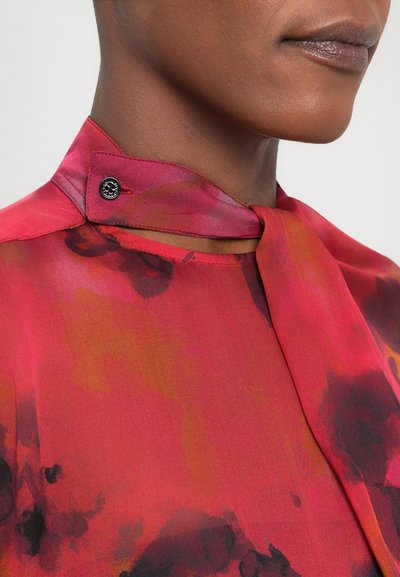 Rood en oranje bloemenblouse met een hoge kraag en een strikdetail. Heeft een knoopaccent en een zachte, vloeiende stofstructuur.