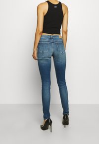 Smala blå jeans i denim, med en midje som sitter något högre och bakfickor med en lätt blekningseffekt. Bärs med svarta högklackade skor.