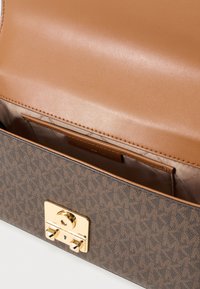 Ruskean kuvioitu käsilaukku, jossa on sileä nahkainen sisusta. Varustettu kullanvärisellä lukolla ja kiiltävillä korttipaikoilla sisällä.