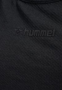 Textil negro con una textura suave, que presenta un logo "hummel" en relieve de un tono coincidente. Se centra en un diseño minimalista y en la durabilidad.