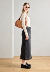 Brun og tan patchwork lædertaske, ribbet cremegul langærmet bluse, sort denim lang nederdel med frynser, og sorte platform loafers.