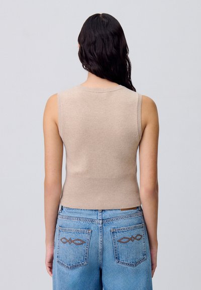 Suéter sin mangas color beige con un escote y dobladillo acanalados. Textura de punto suave. Combinado con jeans de tiro alto color azul claro que presentan costuras decorativas.