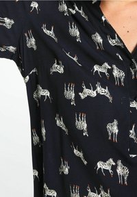 Chemise noire avec un motif zèbre répété et des accents orange, à manches courtes et col. Texture de tissu lisse.