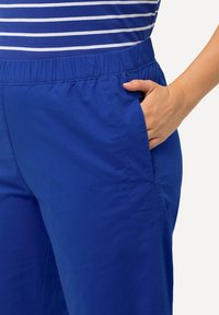 Blå elastiska midjebyxor med sidfickor och en jämn, mjuk textur, som matchas med en randig blå och vit topp.