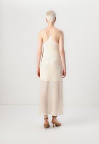 Robe longue sans manches en tissu beige transparent avec un léger scintillement. Dispose de fines bretelles spaghetti et d'une silhouette fluide.