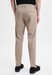 Beige trousers with a tailored design, featuring two back pockets and a slight taper towards the ankle. Smooth fabric texture and clean lines.