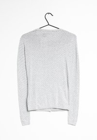 Šedý svetr s dlouhým rukávem z texturované látky, který má vzor malých teček v různých barvách a rovný lem. Visí na černém háčku.