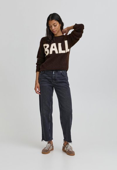 Rjava pletena majica z velikim belim napisom "BALL", kombinirana z visokimi temnimi kavbojkami z raztrganimi robovi in rjavimi supergami.