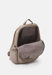 Mochila de tela marrón con un compartimento principal con cremallera y un bolsillo con tapa en la parte delantera. Cuenta con un respaldo acolchado y un asa en la parte superior. Acentos de tela texturada.