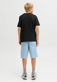 Crna majica kratkih rukava u kombinaciji sa svijetloplavim trapericama. Model nosi sive čarape i sive i plave tenisice.