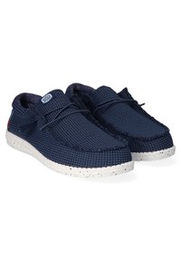 Chaussures en tissu tissé bleu marine avec surface texturée, bout rond et semelle à pois blancs. Présente un détail de lacets et un logo à l'avant.