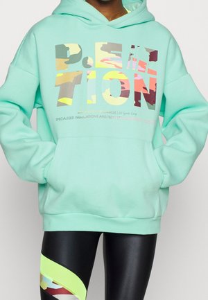 Un hoodie vert menthe avec un motif sur le devant dans diverses couleurs, un legging noir avec des accents néon et des détails en camouflage, et une coupe décontractée.