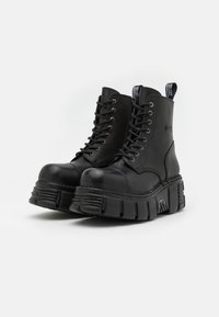 Bottines en cuir noir à lacets avec une semelle épaisse, bout rond et une hauteur de talon supplémentaire. Comprend un détail de couture proéminent et une languette.