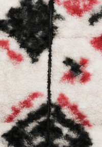 Υφασμα φλις με υφή και λευκή βάση, με μαύρα και κόκκινα διαμαντένια μοτίβα. Κεντρική λεπτομέρεια με μαύρο φερμουάρ.