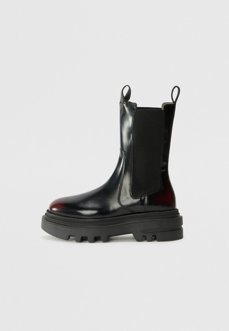 Black leather ankle boot with elastic side panels, rounded toe, and a chunky rubber sole featuring deep treads for traction.