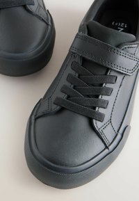 Mustad musta värvi spordijalatsid, millel on siledast nahast pealne, elastsed paelad ja takjapael. Omavad tekstureeritud kummist talla, mis pakub head haaret ja stabiilsust.