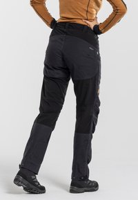 Zwarte outdoorbroeken met versterkte naden, een figuurrijke taille, meerdere zakken en verstelbare manchetten met drukknoopsluitingen. Duurtijdig, waterbestendig materiaal.