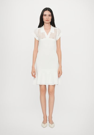 Weißes Strickkleid mit Polo-Kragen, kurzen Ärmeln, schwingendem Saum und Ausschnitten an den Schultern und am unteren Saum. Glatte Textur.