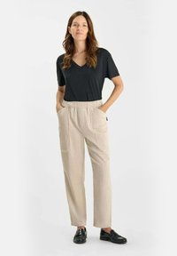 Zwarte v-hals t-shirt gecombineerd met lichtgewicht, beige gestreepte broek met zijzakken en zwarte instappers. Eenvoudig, comfortabel ontwerp.