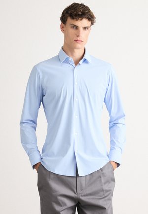 Light blue long-sleeve shirt with a pointed collar, button-down front, and smooth texture, paired with grey trousers.