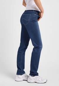 Donkerblauwe denim jeans met een slim fit, met achterzakken en lichte stikselaccenten. Gecombineerd met witte sneakers.