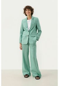 Blazer en lin vert menthe et pantalon large avec un t-shirt blanc en dessous. Comprend deux poches avant et une fermeture à un bouton à l'avant.