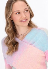 Pull pastel avec un design croisé dans des teintes de rose et de bleu, fabriqué en matériau tricoté doux. Accentué par des colliers superposés.