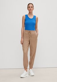 Top in cotone blu a righe, pantaloni jogger beige con vita elastica e tasche laterali, e sneakers bianche. L'outfit presenta una vestibilità comoda e una leggera texture.