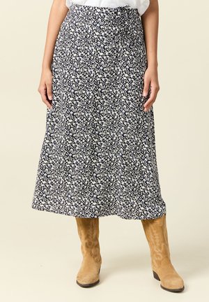 Blumige Midirock in Marineblau mit weißen Blumen; leichtes Material, A-Linien-Form, mit einem Bund und seitlichen Taschen, kombiniert mit beigen Stiefeln.