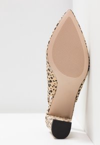 Chaussure à bout pointu avec petit talon bloc, imprimé léopard beige et noir, vue de la semelle sur fond blanc avec un mur.