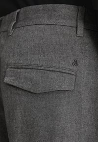 Graue Stoffhosen mit einer Gesäßtasche mit Klappe. Das Material hat eine glatte Textur, und ein kleines Logo ist über der Tasche sichtbar.
