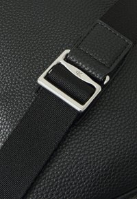 Black textured leather bag featuring a silver metal buckle and black fabric strap, with a smooth surface and subtle grain pattern.