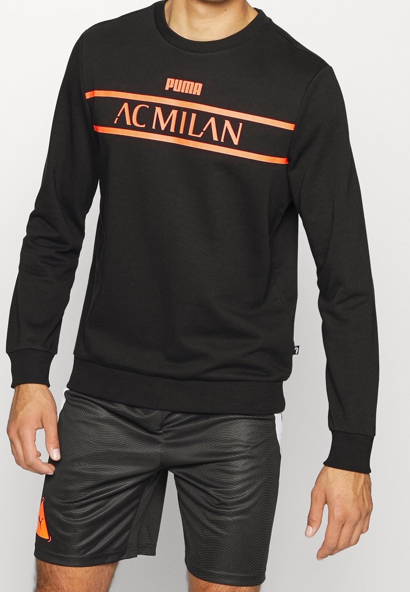 Felpa nera con logo "PUMA" e "AC MILAN" in strisce arancioni brillanti. Le maniche e il collo a coste garantiscono un design aderente.