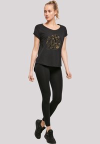 Black short-sleeve t-shirt with a gold graphic design, paired with black leggings and black athletic shoes. Smooth fabric, relaxed fit.