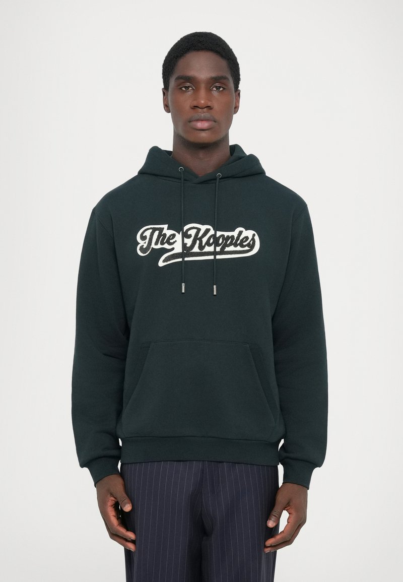 Dark green hoodie features a front kangaroo pocket and white logo text "The Kooples" across the chest. Soft fabric with adjustable drawstrings.