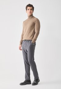 Jersey de cuello alto marrón, diseño ajustado; pantalones grises a medida con bolsillos; zapatos de vestir de cuero negro; estilo minimalista.