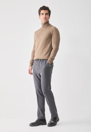 Jersey de cuello alto marrón, diseño ajustado; pantalones grises a medida con bolsillos; zapatos de vestir de cuero negro; estilo minimalista.