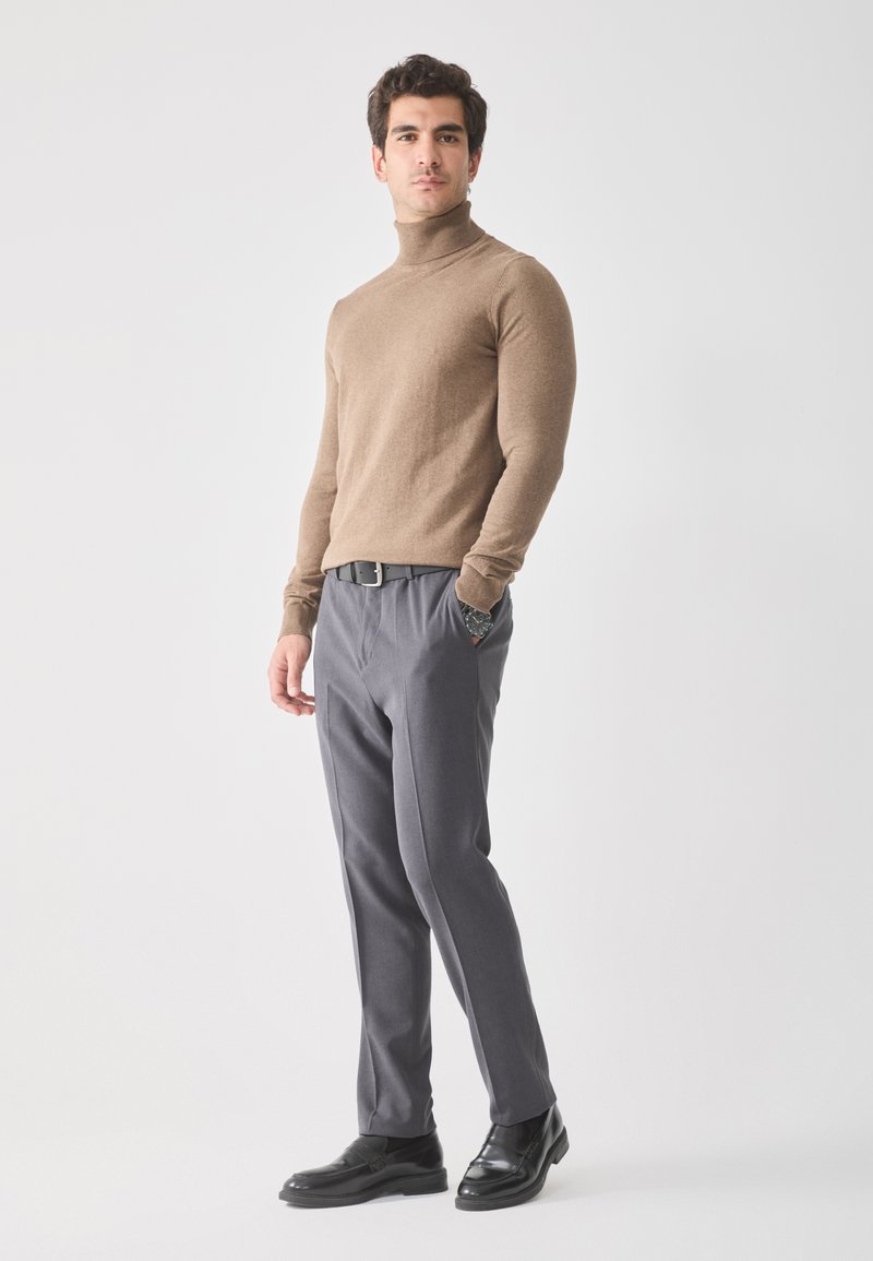 Jersey de cuello alto marrón, diseño ajustado; pantalones grises a medida con bolsillos; zapatos de vestir de cuero negro; estilo minimalista.