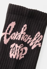Czarna wełniana skarpeta o ryżowym wzorze i wyraźnym różowym logo, które w stylizowanym kroju głosi "Carhartt WIP".