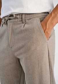 Beige joggingbroek met een gestructureerde stof, elastische tailleband, trekkoord en zijzakken, met een aansluitende pasvorm en een zachte uitstraling.