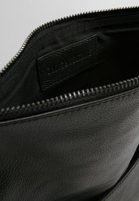 Interno di una borsa a tracolla in pelle nera con una texture liscia, dotata di una chiusura a zip e di un’etichetta con la scritta "Zadig & Voltaire."
