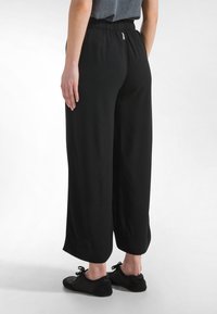 Svarta, vida byxor av mjukt tyg med resår i midjan. Nederkanten är kort, så att svart skor syns.