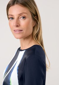 Marineblaues Oberteil mit rundem Halsausschnitt, das ein farbenfrohes abstraktes Design in Weiß, Blau und Grün aufweist. Geschmeidige Textur und figurbetonter Schnitt.