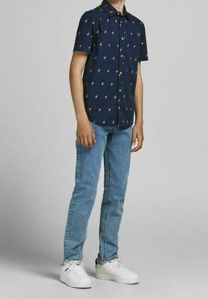 Laivastonsininen lyhythihainen paita, jossa pieni kukkakuosi; vaaleansiniset suoralahkeiset farkut; valkoiset lenkkarit mustilla yksityiskohdilla.