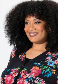 Bloemendessinvstof in levendige kleuren van roze, blauw en groen tegen een zwarte achtergrond; heeft een V-halsontwerp en knoopdetail.